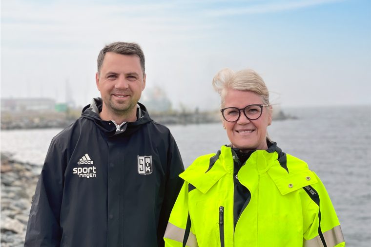En man och en kvinna står bredvid varandra. Bakom syns konturerna av ett fartyg. Vädret består av lätt dimma med en ljusblå himmel som syns uppe i högra hörnet. Båda mannen och kvinnan ser glada ut. De tittar rakt in i kameran.